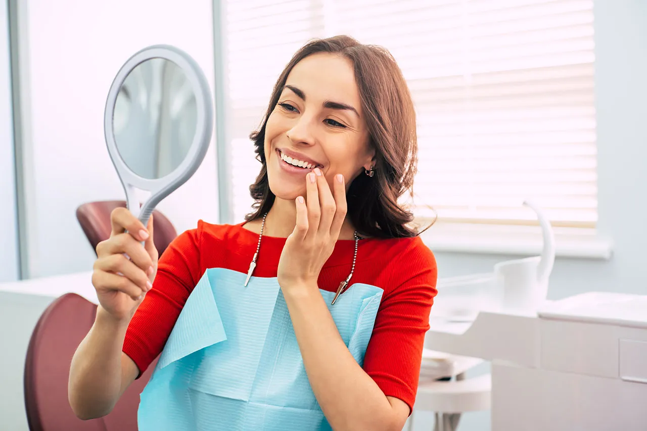 Patient checking her smile in a hand mirror after treatment